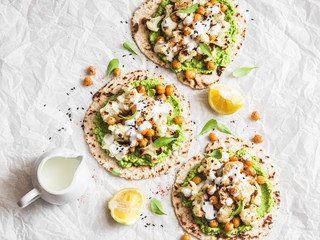 Gluten free flatbread with roasted chickpeas, cauliflower and avocado dip on a light background,...