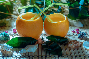 Citrus juice with straw in the orange fruit among green leaves and seashells