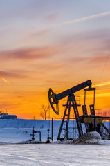 Pump jack and wellhead during sunset in the oilfield. Winter period. Oil and gas concept.