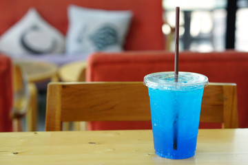 Closeup Cocktail or Tropical Mocktail - Plastic glass of Blue Hawaii Italian Soda with lemon on wooden table and blurred background, Copy Space.