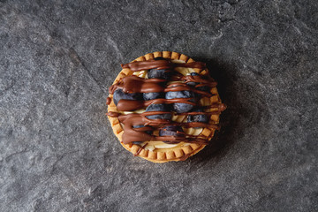 Lemon tartlet, pie, tart with fresh blueberries and milk chocolate over black background. Top view