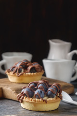 Lemon tartlet, pie, tart with fresh blueberries and milk chocolate on a wooden board, white coffee service, over black background.