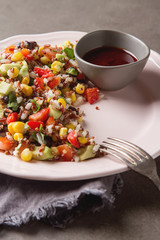 Quinoa salad with corn, tomatoes, avocado, pink sauce on a plate. Gray background.