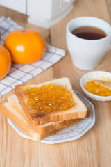 Slice of bread with orange jam and cup coffee.