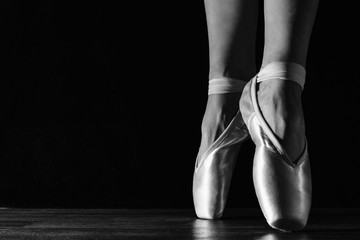 Close-up classic ballerina's legs in pointes on the black floor