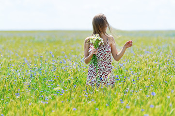 Young beautiful woman with bouquet of camomiles in a dress standing in a cornflower field