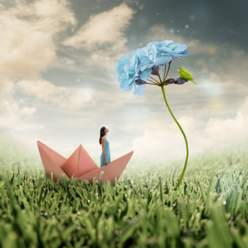 Heavenly photo manipulation of a girl standing alone in an origami paper boat in a magic bright field with sparkling flowers and grass