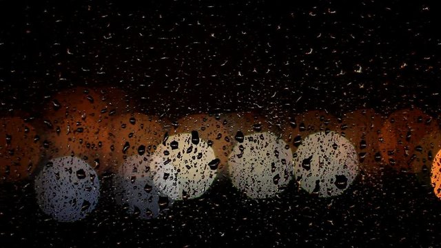 Drops of rain flow down the window glass at night