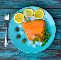 piece of red fish lies on a plate with a lemon, seasonings and vegetables. several pieces of ice
