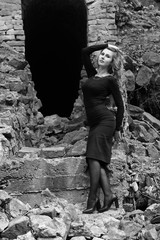 Beautiful sexy and elegant thin young light blonde european woman in total black dress and heels around old ruins in vintage style have a secret in her soul and finding the answer