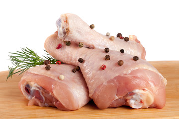 raw chicken drumsticks on a wooden cutting boardn with a sprig of dill and peppercorns white...