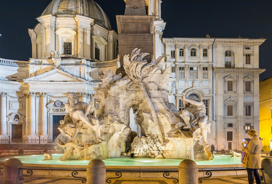 Rome, Italy. The tourist photographs the fountain of the Four Rivers (1651) on Navona square at night with a backlight against the background of the church of Sant'Agnese in Agone (1652)