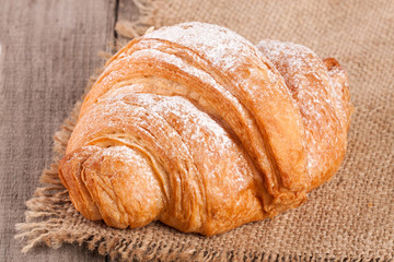 One croissant sprinkled with powdered sugar on a wooden table with napkin