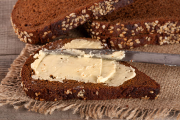 slice of black bread with sesame seeds and butter on an old wooden background