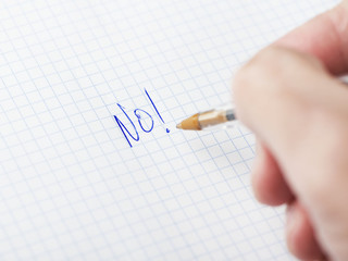Male hand writing no on sheet of paper with pen.