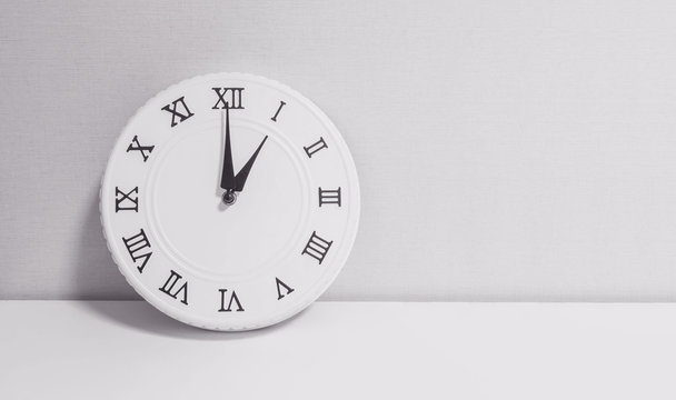 Closeup white clock for decorate in 1 o'clock on white wood desk and wallpaper textured background in black and white tone with copy space