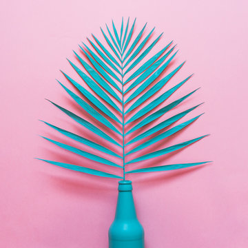 turquoise palm leaf sticking out of a beer bottle on a pink background. fashion food, minimal flat lay.