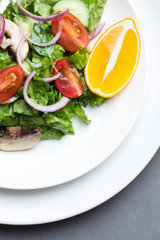 Salad of vegetables and champignons, lemon on white dishes.