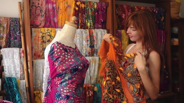 Young slim caucasian woman shopping in Bali shop, looking and taking colorful traditional ceremony balinese clothes kebaya and smile. Shot with Sony a7s on slider indoors