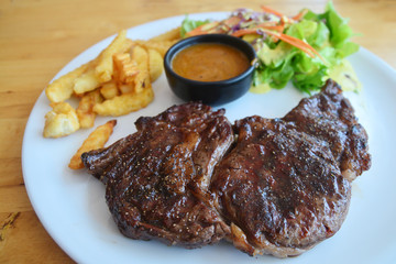 Ribeye steak with salad and French fries on wooden background