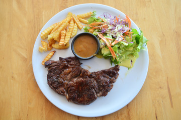 Ribeye steak with salad and French fries on wooden background