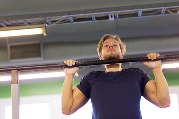 man exercising on bar and doing pull-ups in gym