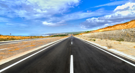 Long highway crossing sunny desert wind under dramatic sky summer day