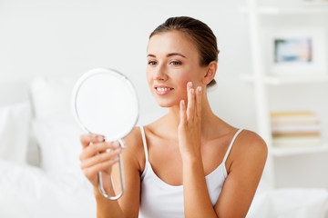 beautiful woman with mirror touching her face skin