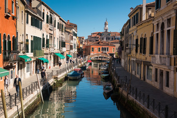 Obraz premium Narrow street with a canal, bridge, boats and tourists in Venice