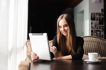 Happy young woman drinking coffee / tea and using tablet computer in a coffee shop