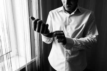 A man in a white shirt buttoning a button on a shirt cuff