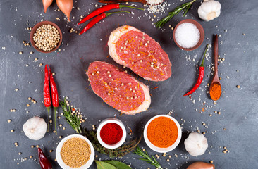 Two beef steaks with white pepper, salt, spices and vegetables on a dark background