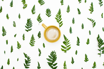 Floral pattern with green leaves, yellow rose petals and a cup of coffee on white background. Flat lay, top view.