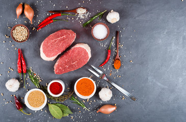 Two beef steaks with spices and vegetables, fork for meat on a dark background