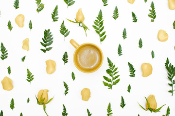 Floral pattern with green leaves, yellow rose petals and a cup of coffee on white background. Flat lay, top view.