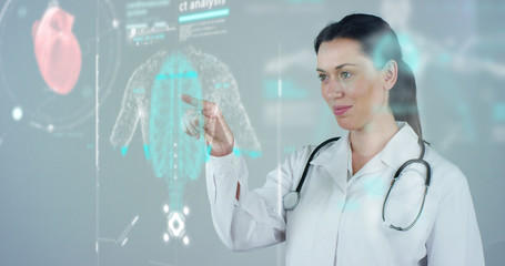 Female doctor with white coat and stethoscope, with holographic tablet represented the patient's body, the heart lungs, muscles, bones. Concept: Futuristic medicine, world assistance, and the future.