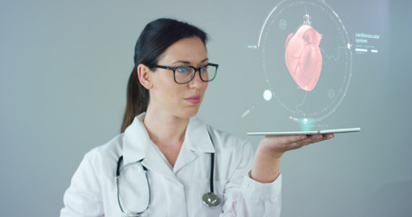 Female doctor with white coat and stethoscope, with holographic tablet represented the patient's body, the heart lungs, muscles, bones. Concept: Futuristic medicine, world assistance, and the future.