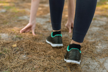 Girl in sports pants and shoes, stands at the start before running, leaning hands, on the nature.