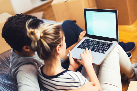 Young couple sitting between boxes and using a laptop