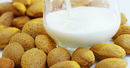 the hand of a boy on a sunny day in the garden pours milk in a transparent cup where milk falls in slow motion . concept of healthy food and breakfast of milk and bisquits or cookies	