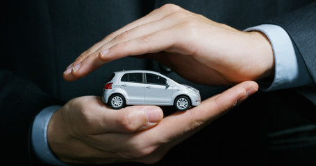 Fototapeta premium A man dressed in a suit and tie, shows a small auto. Concept: car insurance, mechanical, leasing, purchase new and used cars and public garages.