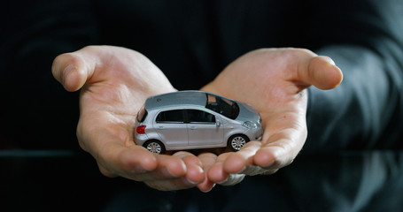 A man dressed in a suit and tie, shows a small auto. Concept: car insurance, mechanical, leasing, purchase new and used cars and public garages.