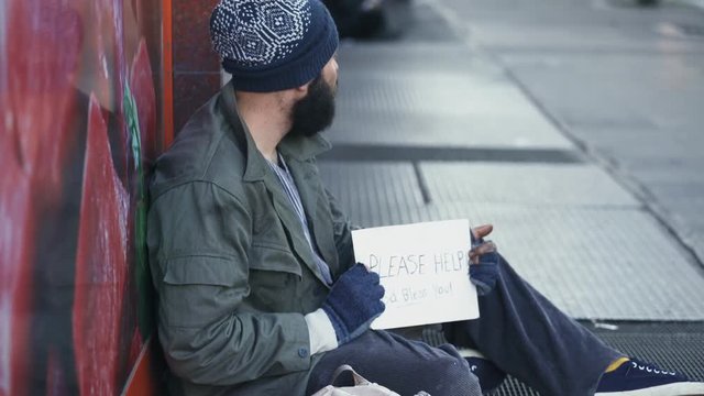 Homeless sitting in the street observes the pedestrians