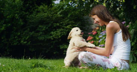 A young woman on a sunny day playing with his Golden Retrivier puppy in the garden giving himself kisses with love and affection	