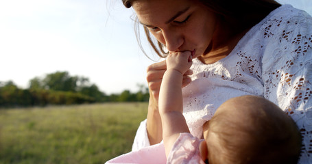 On a sunny day a mother playing with her baby daughter. Mom and daughter are surrounded by greenery and are very happy and releases love and joy grinning and playing with each other