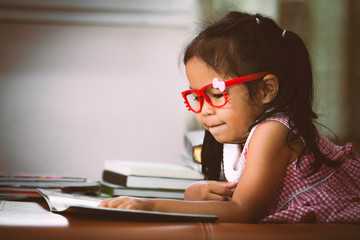 Fototapeta na wymiar Cute asian little put on eyeglasses reading a book in vintage color tone