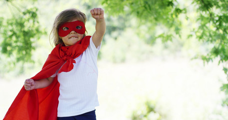 in a beautiful and happy sunny day , a little girl dressed as a super hero makes expressions and...
