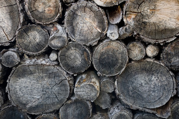 Background: pieces of wood trunk to burn in the fire, cut and stacked near a mountain hut, ruined by the sun and the winter weather, Alps, Switzerland