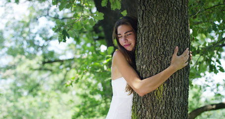 On a sunny day a woman embracing the tree as a sign of love for nature. Nature that she loves and protects because the tree is a symbol of life. The naturalist woman is carefree and smiling