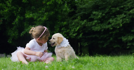 On a sunny spring day a little girl dressed as a ballerina plays with her mom and Golden Retriever puppy in the garden and everyone smiles like a happy family	